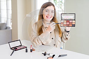 Beautiful young woman using make up cosmetics applying color from palete with a happy face standing and smiling with a confident
