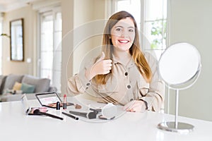 Beautiful young woman using make up cosmetics doing happy thumbs up gesture with hand