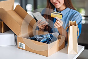 A beautiful young woman using mobile phone and credit card for online shopping with shopping bag and postal