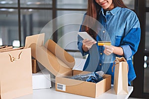 A beautiful young woman using mobile phone and credit card for online shopping with shopping bag and postal