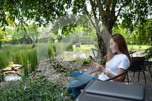 A beautiful young woman using mobile phone with laptop computer on the table in the park