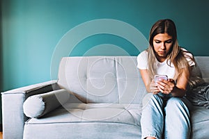 Beautiful young woman using smartphone while relaxing on sofa at living room