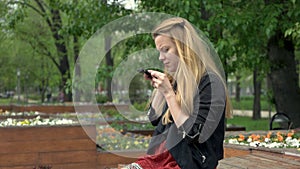 Beautiful young woman using a smartphone in summer park and doing selfie