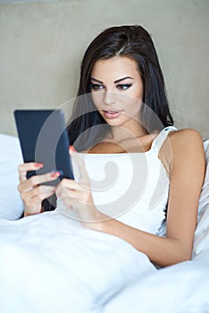 Beautiful young woman using a tablet in bed