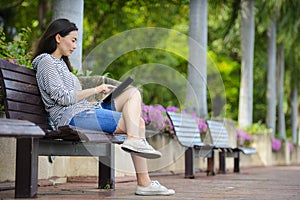 Beautiful young woman using tablet computer on a bench in the park