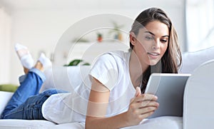 Beautiful young woman using tablet sitting on sofa at home at living room.