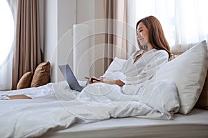 A beautiful young woman using and working on laptop computer while lying on bed at home