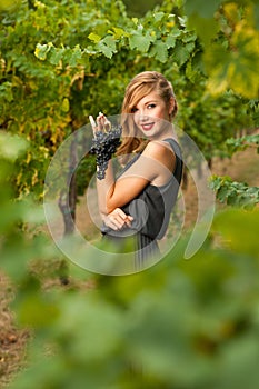 Beautiful young woman in vineyard holding a grape