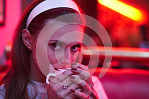 Beautiful young woman in vintage dress in red light cafe drinking coffee