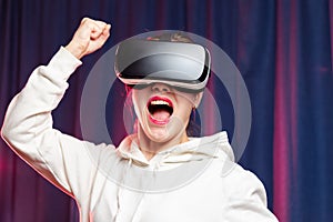 A beautiful young woman in virtual reality glasses plays video games and a white hoodie on a purple background. Modern technologie