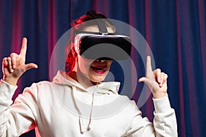 A beautiful young woman in virtual reality glasses plays video games and a white hoodie on a purple background. Modern technologie