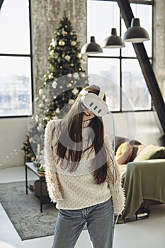 A beautiful young woman in a virtual reality headset against the backdrop of a Christmas tree