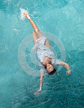 Beautiful young woman with vitiligo depigmentation in white evening dress swimming elegant floating weightless in the pool in