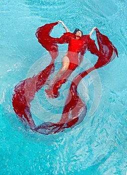 Beautiful young woman with vitiligo disease in red dress, evening dress floating weightlessly elegant in the water in the pool