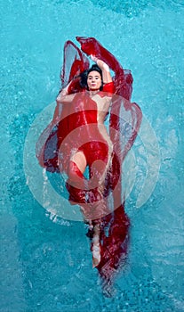 Beautiful young woman with vitiligo disease in red evening dress, floating weightlessly elegant in the pool