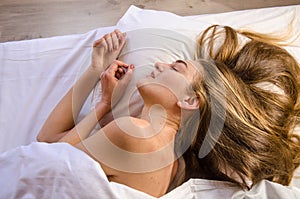 Beautiful young woman wakes up in the morning in white bed in the rays of the sun, she has lush wavy blonde, golden hair