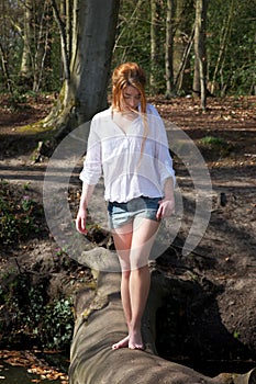 Beautiful young woman walking across a log over stream