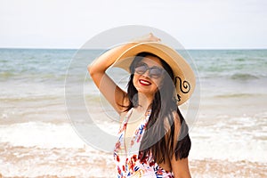 Beautiful young woman walking along the beach with a hat to protect herself from the sun. The woman is enjoying her trip to a