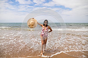 Beautiful young woman walking along the beach with a hat to protect herself from the sun. The woman is enjoying her trip to a