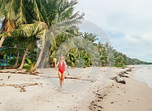 Beautiful young woman walking on the beach along palm trees holding coconut in Koh Phangan, Thailand