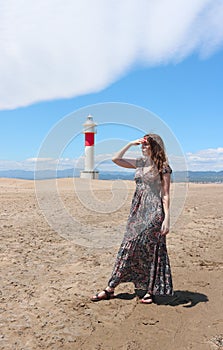 Beautiful Young woman walking on the beach, and a lighthouse in the background