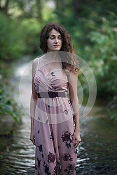 Beautiful young woman walking through the forest river.