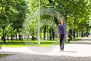 Beautiful young woman walking in green summer park