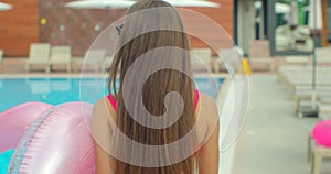 Beautiful young woman walking by the pool holding sprinkled pink inflatable flamingo float in summer. Pool summer