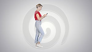 Beautiful young woman walking and reading text message on her mobile phone on gradient background.