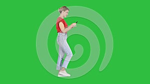 Beautiful young woman walking and reading text message on her mobile phone on a Green Screen, Chroma Key.