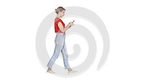 Beautiful young woman walking and reading text message on her mobile phone on white background.