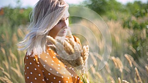 Beautiful young woman walks in the field collects a bouquet of flowers and spikelets. Portrait of attractive female on grass at su