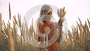 Beautiful young woman walks in the field collects a bouquet of flowers and spikelets. Portrait of attractive female on grass at su