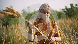 Beautiful young woman walks in the field collects a bouquet of flowers and spikelets. Portrait of attractive female on grass at su