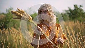 Beautiful young woman walks in the field collects a bouquet of flowers and spikelets. Portrait of attractive female on grass at su