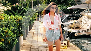 Beautiful young woman walks by moored luxury yachts on a summer day