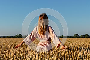 Beautiful young woman walks in a wheat field. Portrait from the back of an attractive girl in a pink dress.