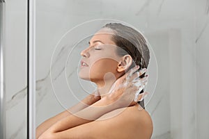 Beautiful young woman washing hair in shower at home