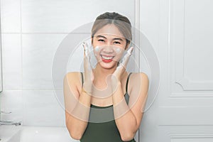 Beautiful young woman washing her face foam in a bathroom