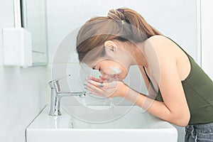 Beautiful young woman washing her face splashing water in a bathroom