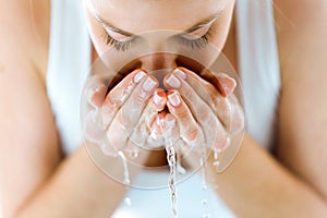 Beautiful young woman washing her face splashing water in a home bathroom.