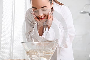 Beautiful young woman washing her face with water in bathroom