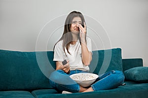 Beautiful young woman watching melodrama eating popcorn crying on the sofa at home