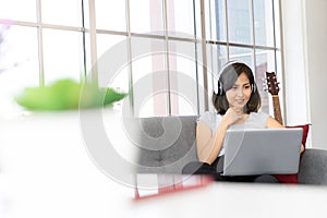 Beautiful young woman wear headphones and using laptop while sitting on sofa at home, work from home, conference meeting