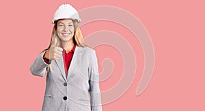 Beautiful young woman wearing architect hardhat doing happy thumbs up gesture with hand