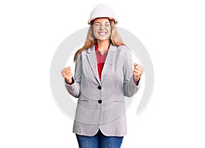 Beautiful young woman wearing architect hardhat excited for success with arms raised and eyes closed celebrating victory smiling
