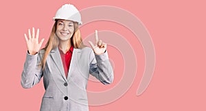 Beautiful young woman wearing architect hardhat showing and pointing up with fingers number seven while smiling confident and