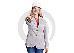 Beautiful young woman wearing architect hardhat smiling friendly offering handshake as greeting and welcoming