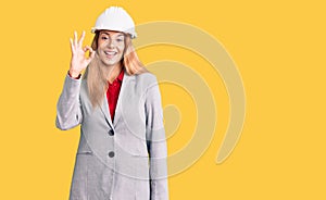 Beautiful young woman wearing architect hardhat smiling positive doing ok sign with hand and fingers