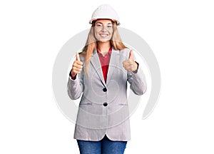 Beautiful young woman wearing architect hardhat success sign doing positive gesture with hand, thumbs up smiling and happy